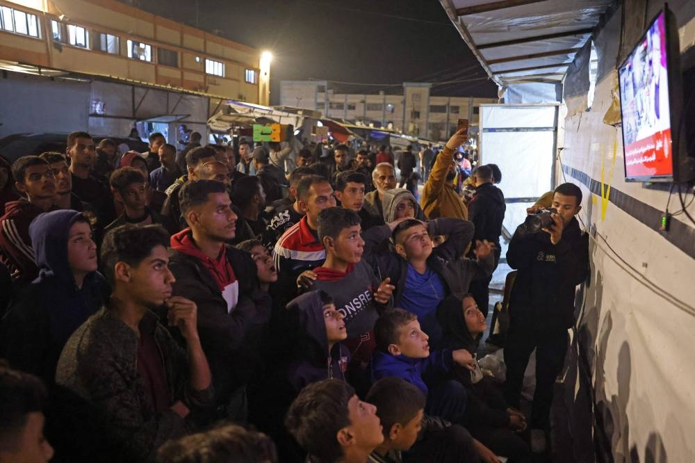 People watch a television along a street in Khan Yunis in the southern Gaza Strip on January 15, 2025, amid the ongoing war in the Palestinian territory between Israel and Hamas. Thousands of Gazans celebrated on January 15 as news spread that a ceasefire and hostage release deal had been reached between Israel and Hamas, aimed at ending more than 15 months of war in the Palestinian territory. (Photo by BASHAR TALEB / AFP)