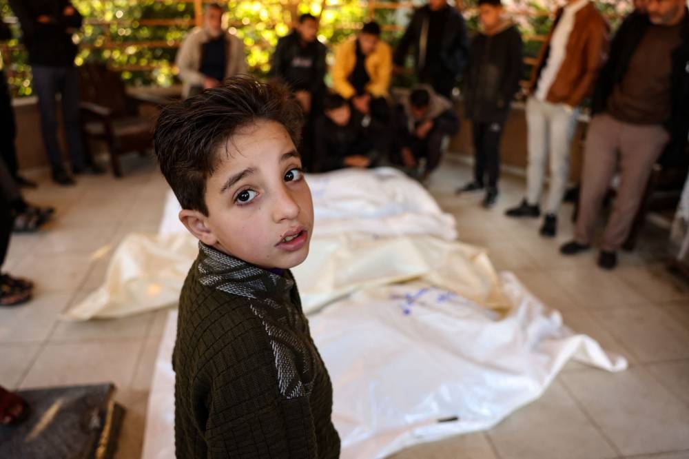 A child stands beside the bodies of four members of the Palestinian al-Qadra family (parents and their two children) killed in an Israeli strike that hit their tent north of Khan Yunis in the southern Gaza Strip, in the yard of the Nasser hospital on Saturday, a day before the expected implementation of a ceasefire agreement between Israel and Hamas. AFP