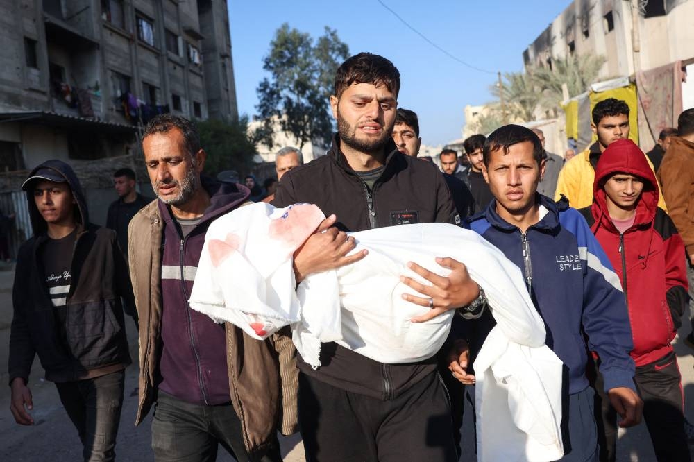 A relative carries the body of a child, one of four members of the Palestinian al-Qadra family (parents and their two children) killed in an Israeli strike that hit their tent north of Khan Yunis in the southern Gaza Strip, in the yard of the Nasser hospital on Saturday, a day before the expected implementation of a ceasefire agreement between Israel and Hamas. AFP