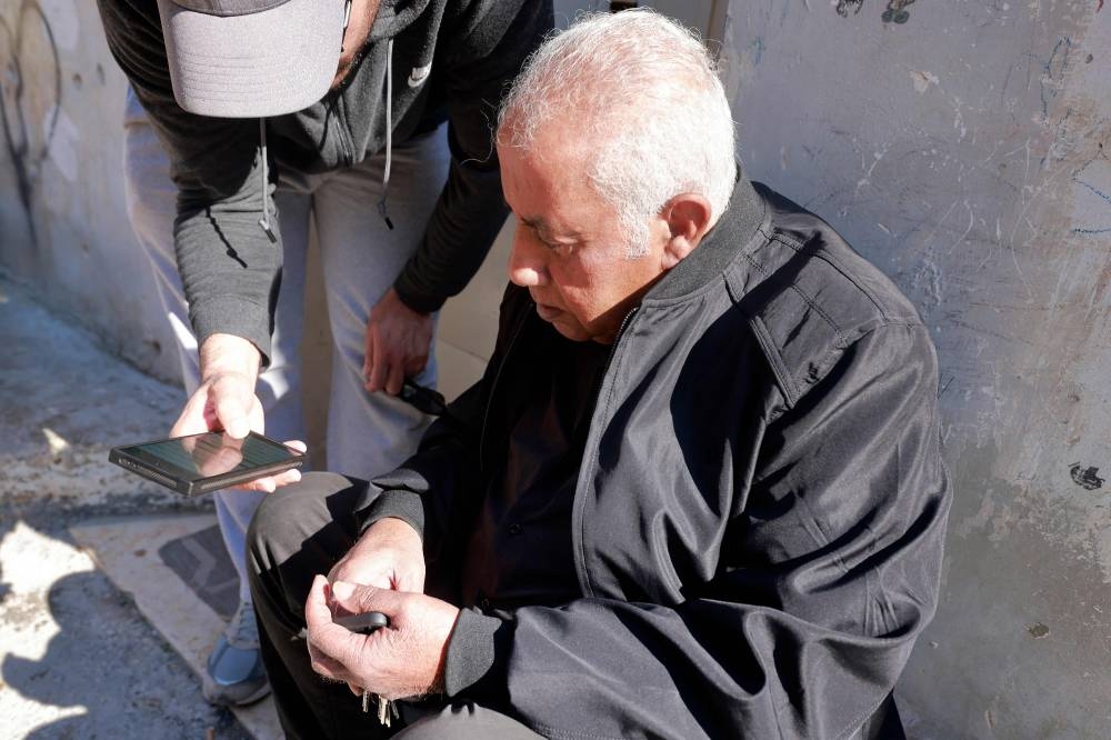A man holds a phone for the uncle of Palestinian prisoner Zakaria Zubeidi to check a list of people set to be released tomorrow during a prisoner exchange as part of the deal to release Israeli hostages held captive in the Gaza Strip by Palestinian militants, as he sits in the Jenin camp for Palestinian refugees in the occupied West Bank on January 18, 2025. The ceasefire in the Gaza war will begin at 0630 GMT on January 19, mediator Qatar said after Israel's cabinet voted to approve the truce and hostage-prisoner release deal. In more than 15 months of war between Hamas Palestinian militants and Israel, there has been only one previous truce, for one week, in November 2023 that also saw a hostage-prisoner exchange. (Photo by Jaafar ASHTIYEH / AFP)