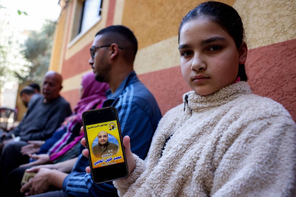 The daughter of Mohammad al-Halabi, Palestinian aid worker and Gaza operations manager for ecumenical Christian humanitarian aid organisation World Vision International -- who was arrested at the Erez border crossing with Israel in 2016, holds a phone showing his picture as she sits with family members after they are notified of his release at a house in Zawayda in the central Gaza Strip on Saturday. AFP
