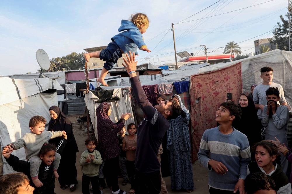 A man throws a child into the air as displaced Palestinians celebrate at a tent camp following a ceasefire between Israel and Hamas, in Deir Al-Balah in the central Gaza Strip, on Sunday. REUTERS
