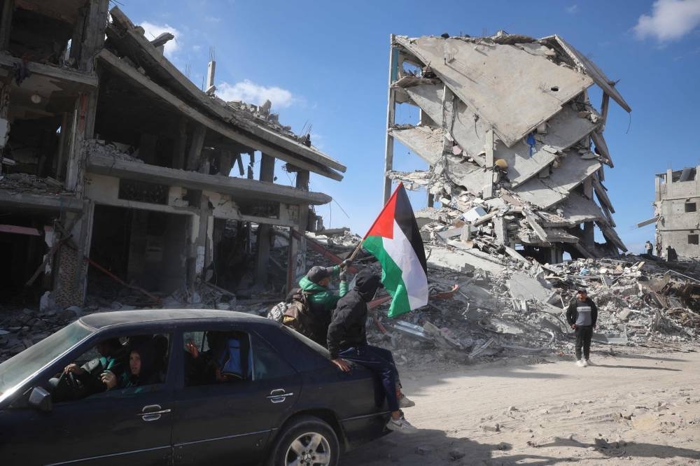 Palestinians lift their national flag as they sit on the trunk of a car driving in a ruined neighbourhood of Gaza's southern city of Rafah on Monday, as residents return following a ceasefire deal a day earlier between Israel and the Palestinian Hamas group. 