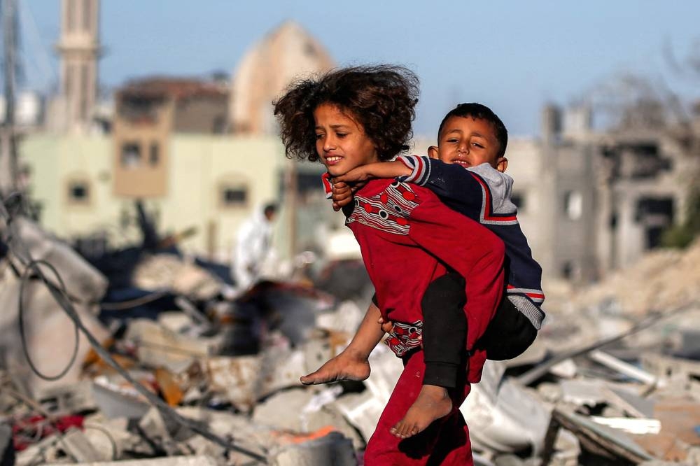 A girl carries a boy on her back as she walks past rubble and debris in Rafah in the southern Gaza Strip on Tuesday, as residents return following a ceasefire deal in the war between Israel and Hamas. AFP