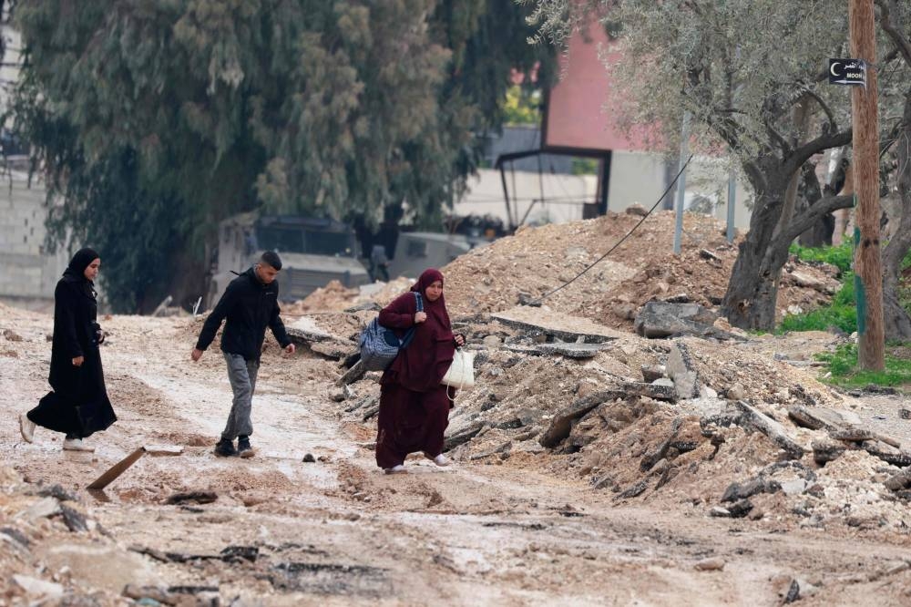 People walk on a destroyed road as they leave Jenin during a large-scale Israeli army raid, in the occupied West Bank, on Friday. A Palestinian official said hundreds of people began leaving their homes in a flashpoint area of the occupied West Bank on Thursday, as Israeli forces pressed a deadly operation there.  AFP
