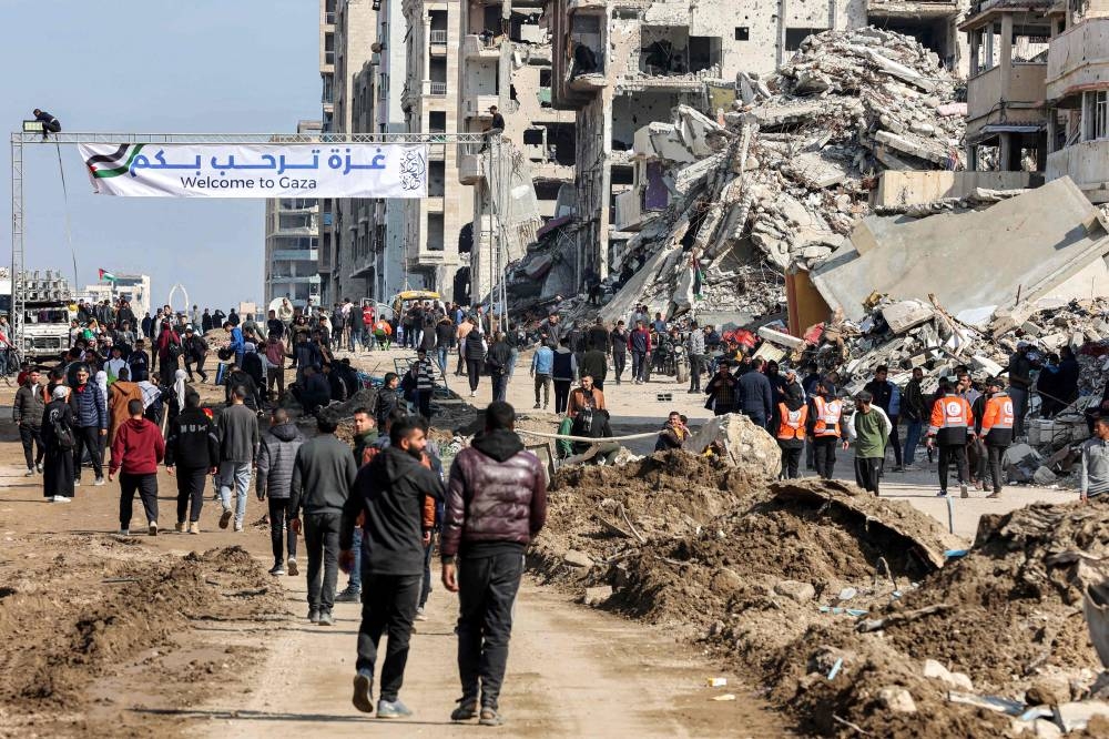 People gather by a banner welcoming people near the rubble of a collapsed building along Gaza's coastal al-Rashid Street for people to cross from the Israeli-blocked Netzarim corridor from the southern Gaza Strip into Gaza City on Sunday. AFP