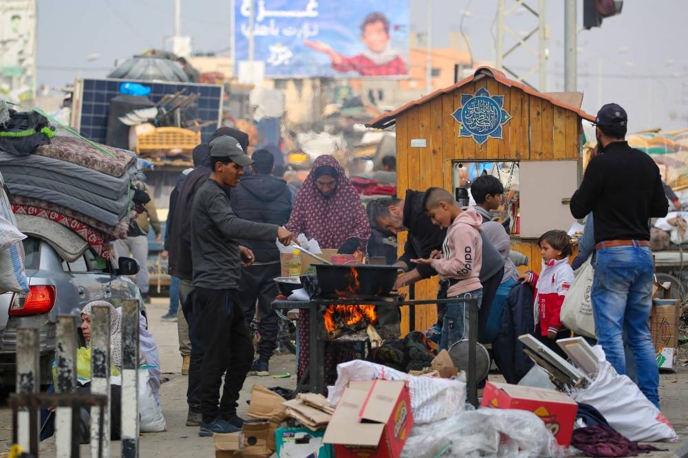 Palestinians cook next to cars loaded with their belongings along Salah al-Din road in Nuseirat as they make their way to the northern part of the Gaza strip on Tuesday. AFP