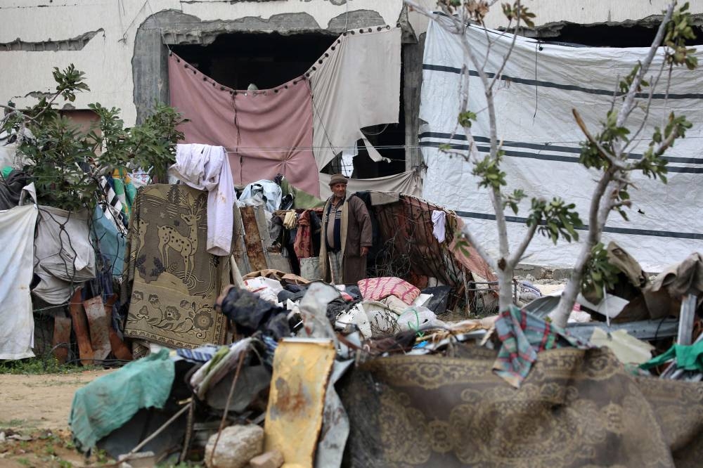 A Palestinian man stands amid scattered belongings in front of a makeshift shelter in the war-devastated Bureij refugee camp in the central Gaza Strip Friday.