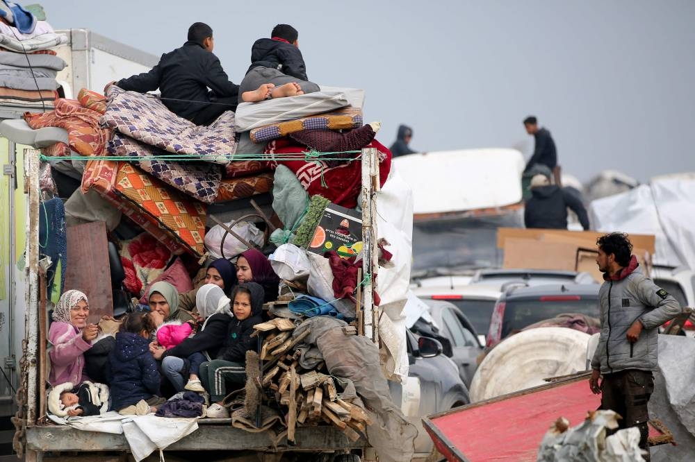 Displaced Palestinians sit in the back on a loaded truck on Salah al-Din road in the central Gaza Strip, Monday