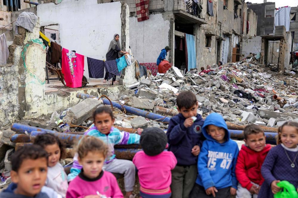 A woman standing by clothes drying on a laundry line watches kids standing by the rubble of a destroyed building at the Shati camp for Palestinian refugees north of Gaza City on Tuesday. AFP