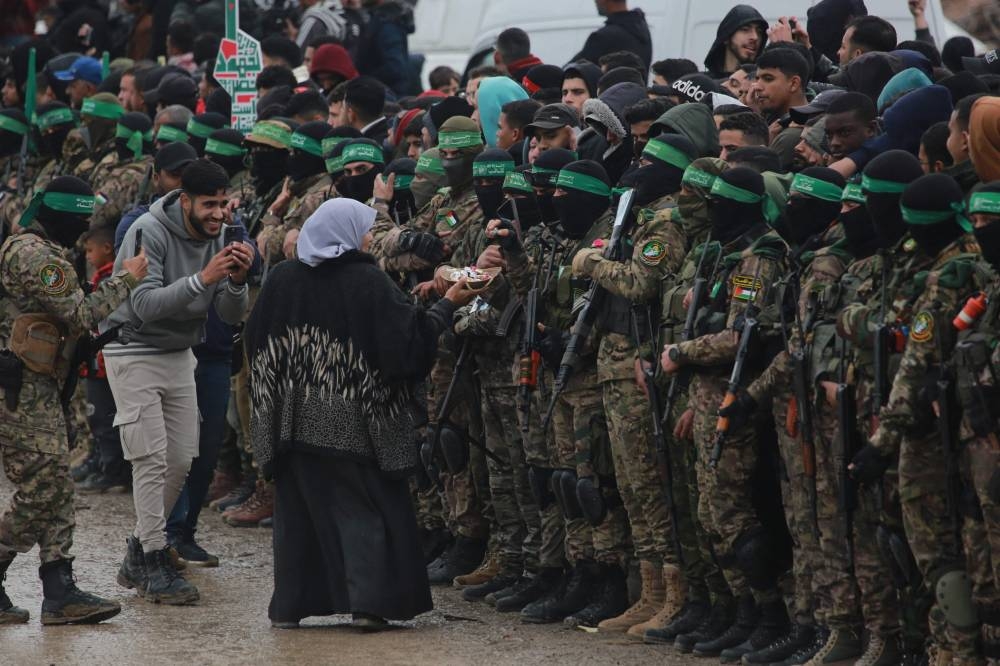 A Palestinian woman offers sweets to Hamas fighters as they gather with people in Nuseirat in the central Gaza Strip, during preparations for the release of three Israeli hostages as part of the seventh hostage-prisoner swap, on Saturday. AFP