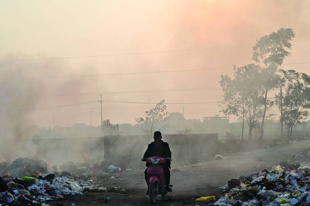 
A man riding a motorbike amid smoke from a burning garbage dump on the outskirts of Hanoi. 