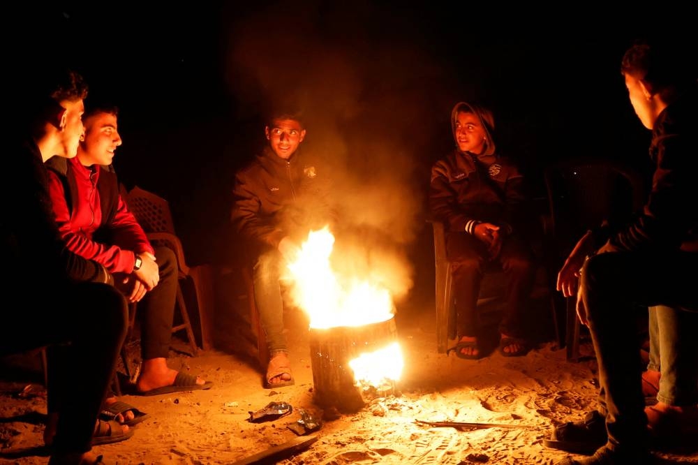 Palestinians sit around a fire during a power cut, in Rafah in the southern Gaza Strip, on Sunday. REUTERS
