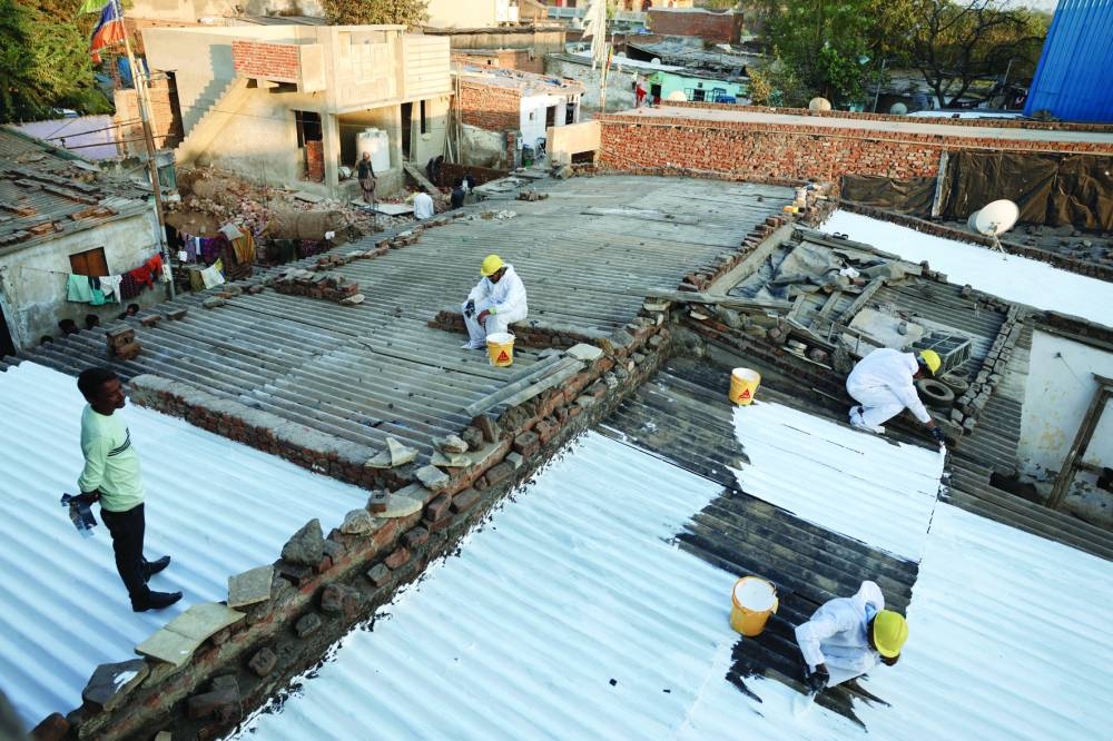 
Painters apply liquid-applied membrane coating that according to the authorities helps to bring down the temperature inside the shanties at a slum in Ahmedabad. (Reuters) 