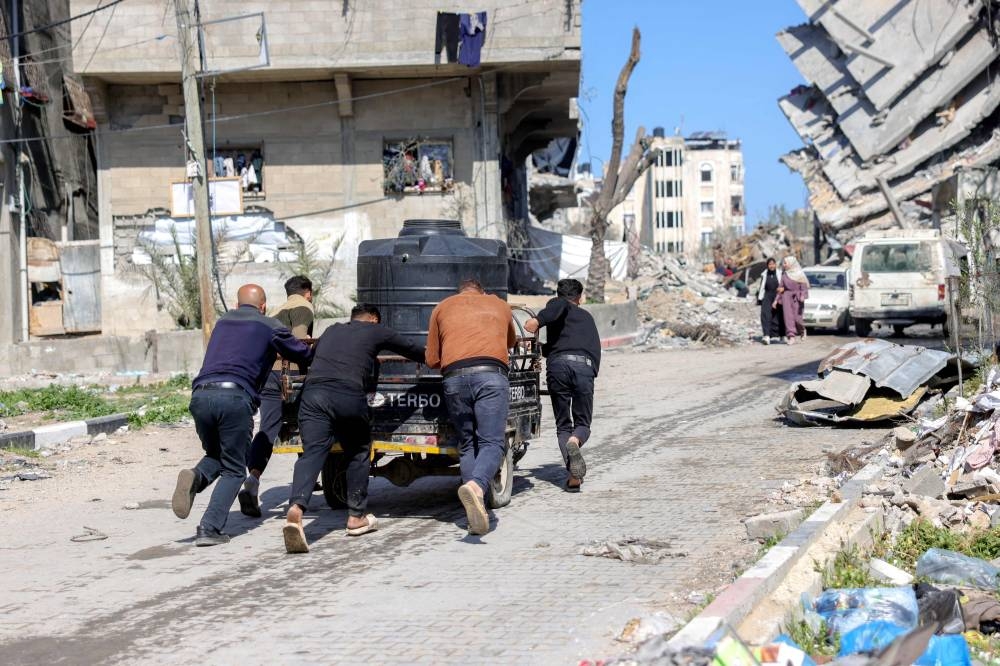 Palestinians push a vehicle carrying a water tank uphill at a displacement camp west of Jabalia city in the northern Gaza Strip, on Tuesday. AFP