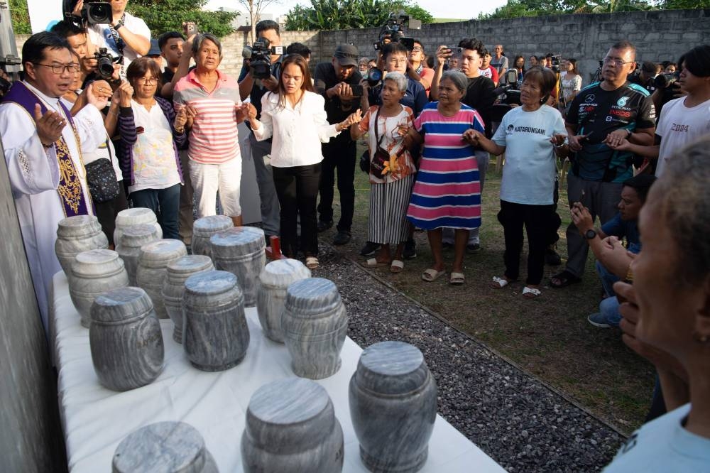 Catholic priest Father Flavie Villanueva (L), head of "Program Paghilom", a group helping relatives of victims of former Philippine president Rodrigo Duterte's war on drugs, leads prayers besides urns containing the ashes of victims during a funeral ceremony at a cemetery in Manila on Wednesday. AFP