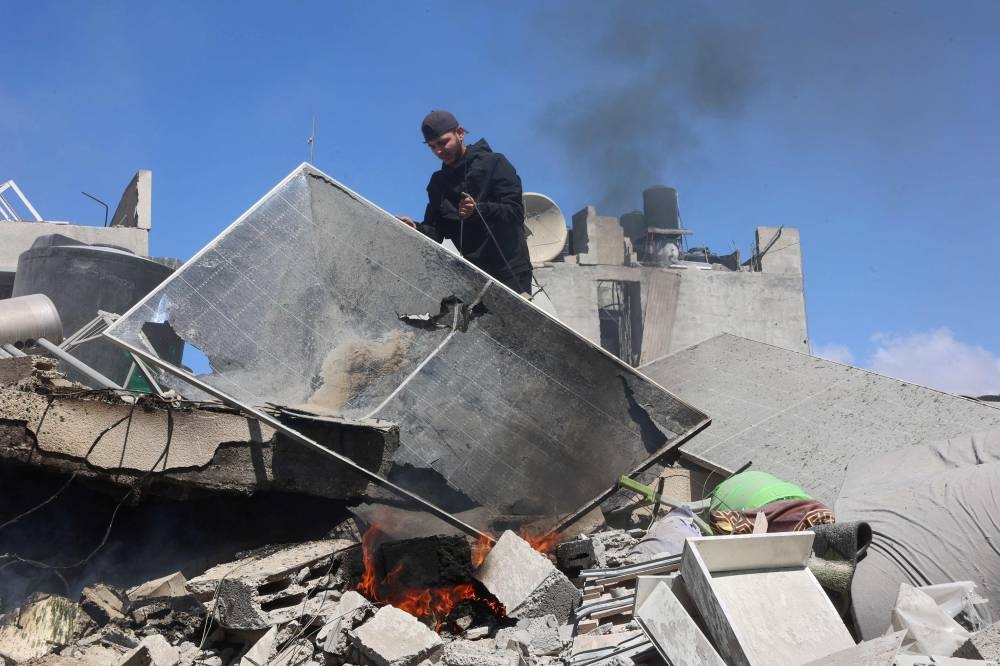 A Palestinian man clears rubble around a fire in the rubble of the Elias Tarazi family house, after it was destroyed in an Israeli strike in al-Sabra neighbourhood in Gaza City on Wednesday. AFP