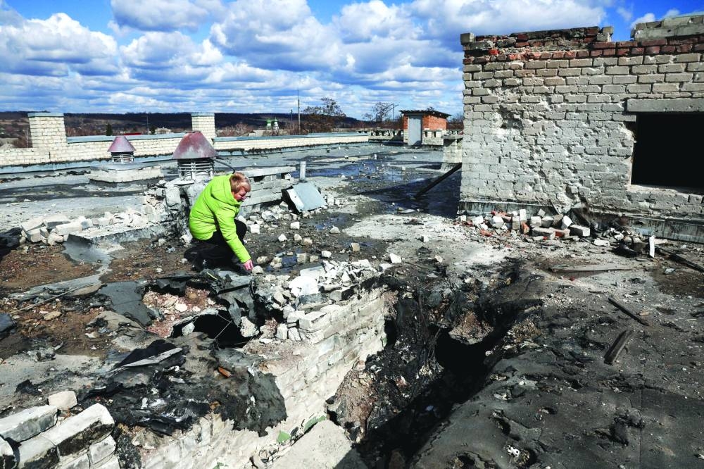 Olha Kyzym, Head of the Department of Education of the Pechenihy village council, picks up a piece of shrapnel of a Shahed drone on the rooftop of the village school, bombed two days prior in an overnight strike in Ukraine, Wednesday.