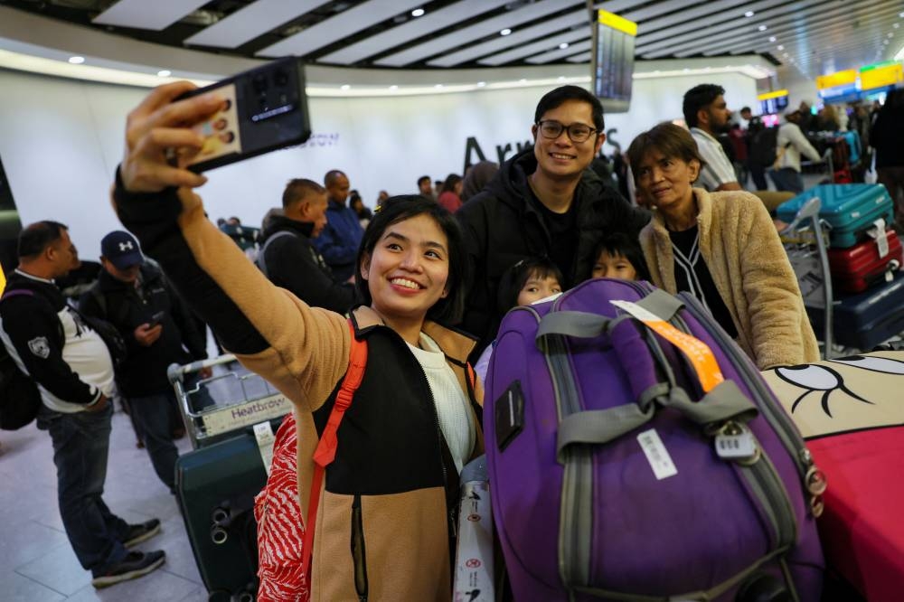A family takes a selfie as they arrive at Terminal 4 of the Heathrow International Airport, a day after a fire at a nearby electrical substation wiped out the power at the airport, near London, on Saturday. REUTERS