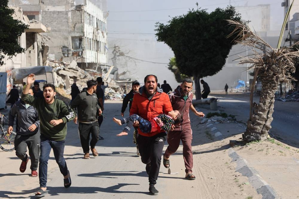 Palestinians rush an injured girl away from the site of Israeli strikes on a makeshift displacement camp in central Gaza City, on Sunday. AFP