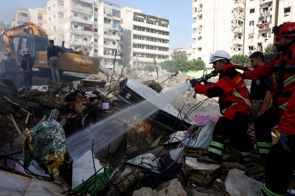 A member of the search and rescue team from the Lebanese Civil Defense sprays water from a hose at the site of an Israeli strike, in Beirut southern suburbs, on Friday. REUTERS
