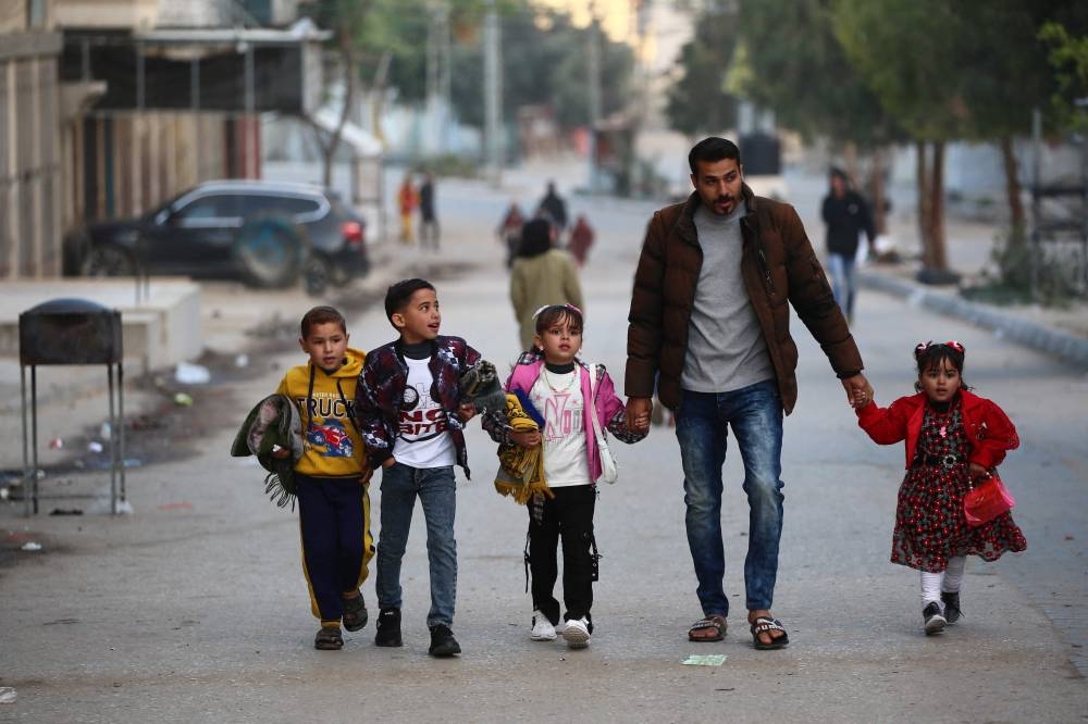 A Palestinian man walks with his children after Eid al-Fitr prayers, which marks the end of the holy fasting month of Ramadan, in the Nuseirat camp for Palestinian refugees in the central Gaza Strip, on Sunday. AFP