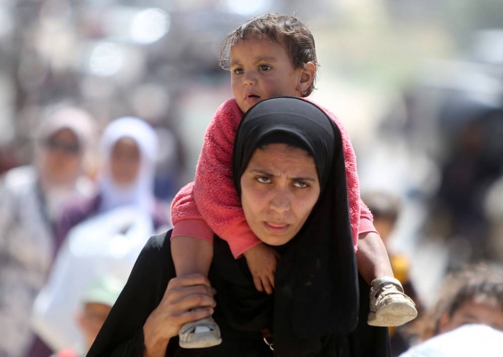 A woman carries a child, as Palestinians make their way after fleeing areas around the southern city of Rafah, following an Israeli evacuation order, in Khan Younis in the southern Gaza Strip, on Monday. REUTERS