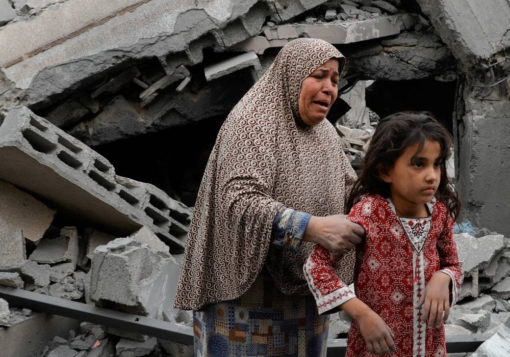 A woman holds a child as Palestinians inspect the site of an Israeli strike on a house, in Khan Younis in the southern Gaza Strip on Tuesday. REUTERS