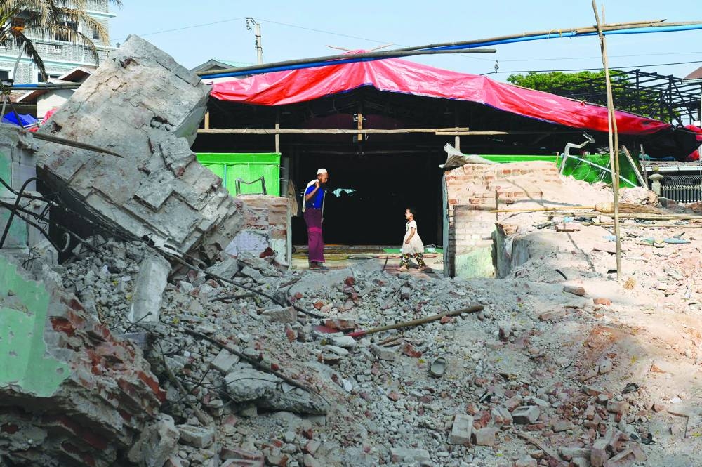 People walk past a temporary mosque next to debris of the former mosque in Mandalay following the devastating March 28 earthquake.