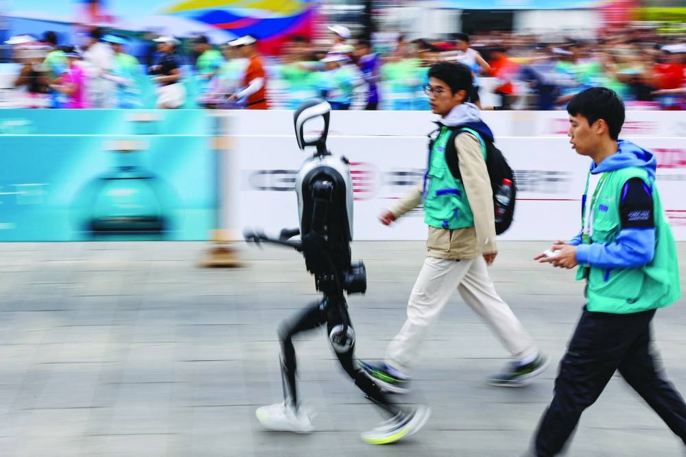 Engineers run with a humanoid robot Kuavo as it participates, along with human runners, in the E-Town Half Marathon & Humanoid Robot Half Marathon in Beijing.