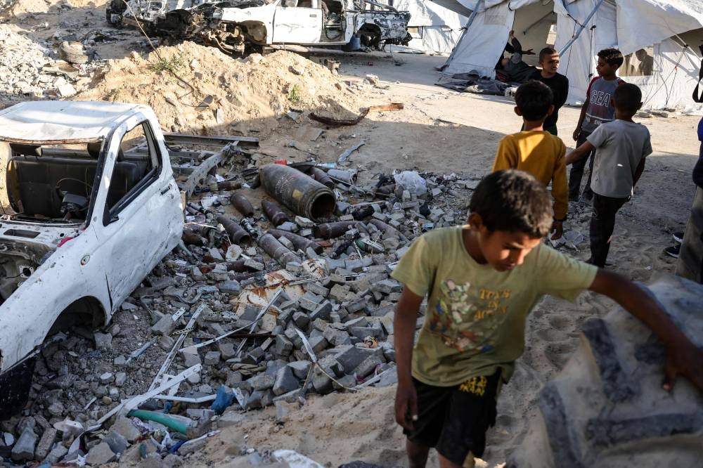 Palestinian children gather near unexploded ordnance, near a shelter in Gaza City on Saturday 
