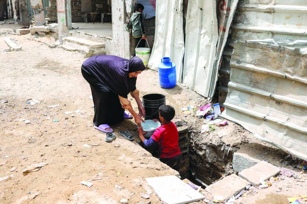 A woman helps a boy lift up a container filled with water from the remaining water still left in underground pipes, in Beit Lahia in the northern Gaza Strip on Thursday 