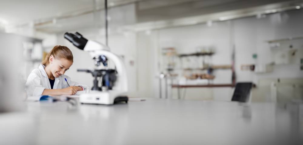 education, science and children concept - girl studying chemistry at school laboratory and writing to workbook