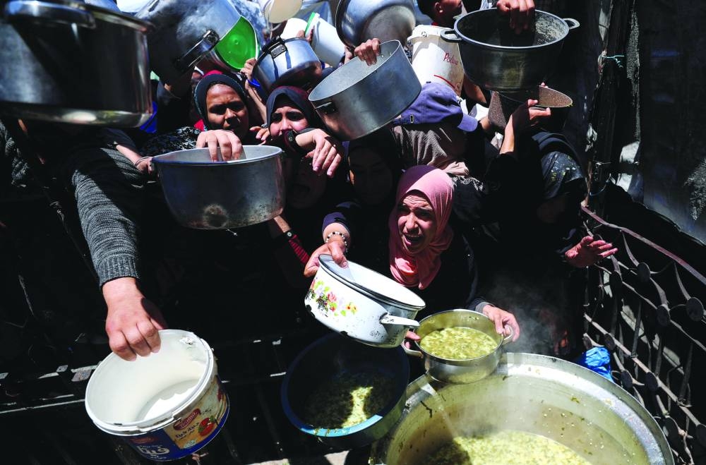 
Palestinians receive food cooked by a charity kitchen in Beit Lahia, northern Gaza Strip, yesterday. 