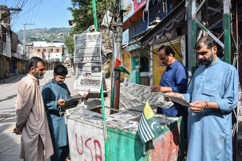 Residents read morning Urdu newspapers with the headline 'The ceasefire between Pakistan and India' on a roadside in Muzaffarabad, the capital of Pakistan-administered Kashmir, on Sunday. AFP