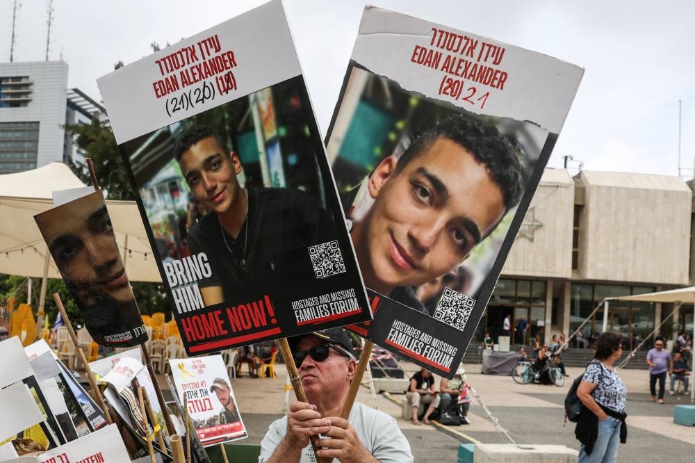 A person holds the pictures of the hostages, on the day Israeli-American hostage Edan Alexander is expected to be released from captivity by Hamas in Gaza, in Tel Aviv, Israel on Monday. REUTERS