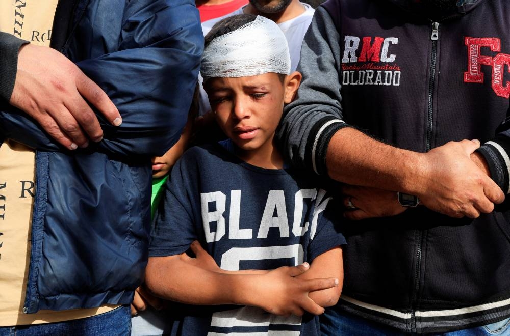 Injured Palestinian child, Yousef Al-Bayouk, prays over his brothers, Moath and Moataz, who were killed in Israeli strikes, as mourners attend their funeral at Nasser hospital in Khan Younis, southern Gaza Strip, on Thursday. REUTERS