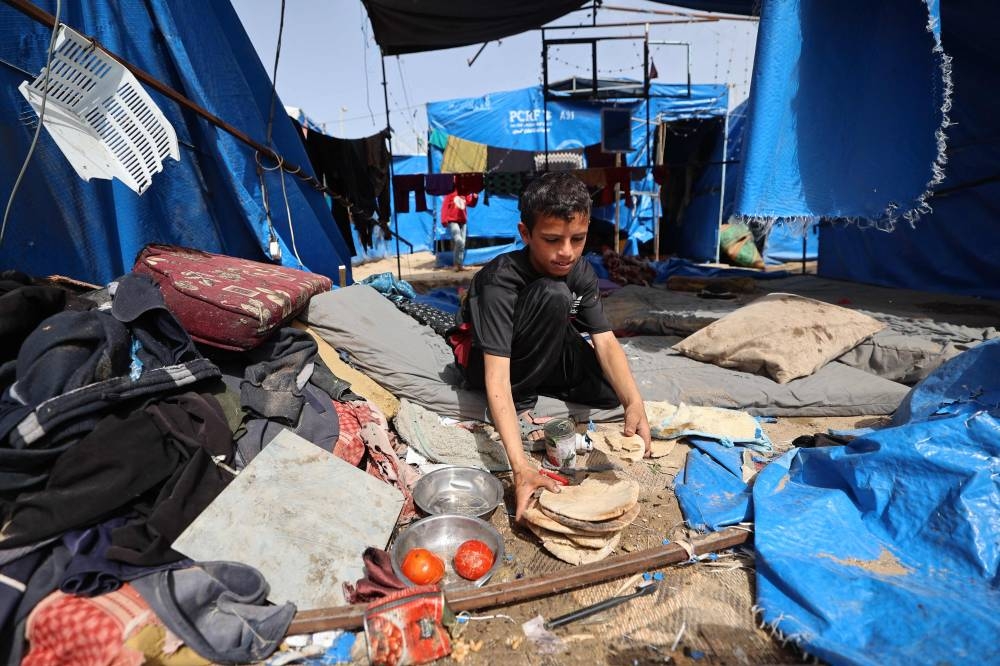 A Palestinian boy collects loaves of old pita bread in a damaged tent following overnight Israeli airstrikes that reportedly hit tents for displaced Gazans outside the Al-Aqsa Martyrs hospital in Deir el-Balah in the central Gaza Strip, on Saturday. AFP