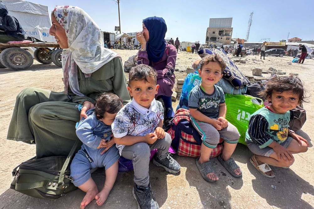 Palestinians sit with their belongings awaiting transportation following Israeli evacuation orders for Khan Yunis on Monday. AFP
