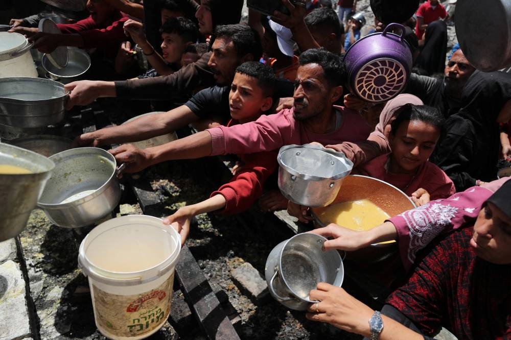 Palestinians wait to receive food cooked by a charity kitchen, in Jabalia, in the northern Gaza Strip on Monday. REUTERS
