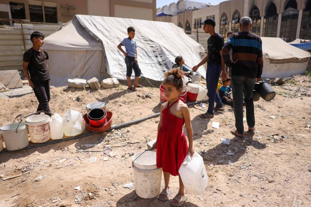 A girl holds plastic containers as displaced Palestinians collect water at a camp in Gaza City, on Tuesday. AFP