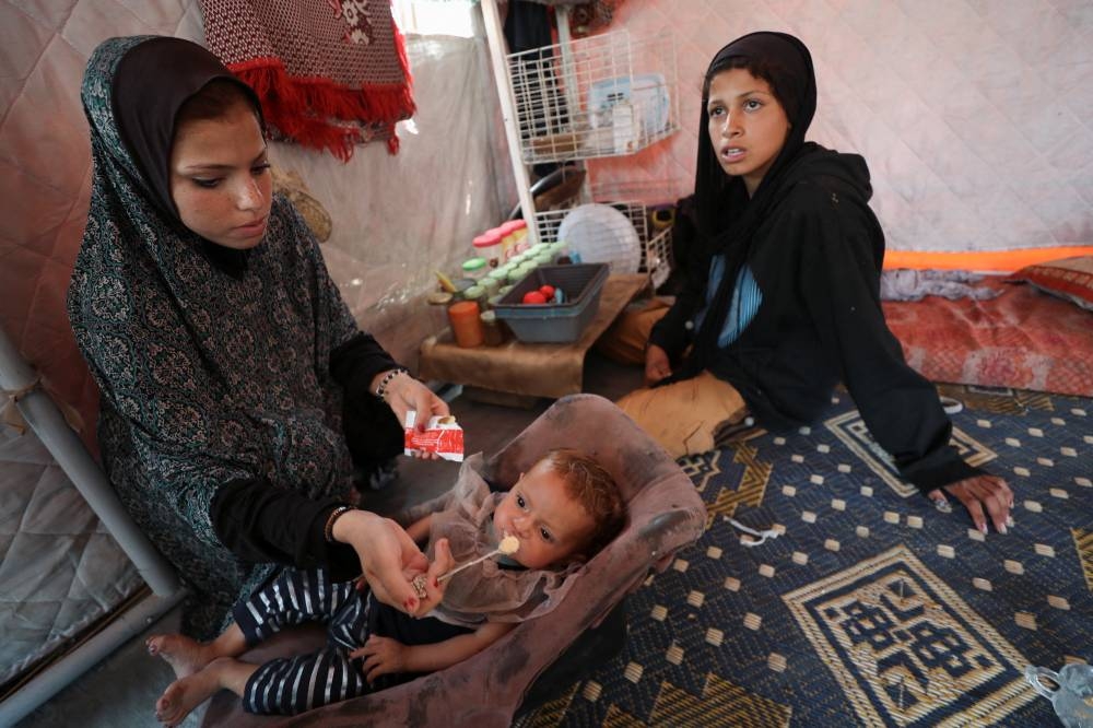 A Palestinian girl feeds her sister inside the tent that they took shelter after being displaced, in Gaza City, May 22, 2025. REUTERS/Mahmoud Issa