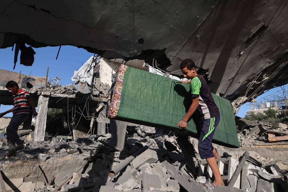 Palestinian boys carry a mattress from inside a house targeted in an Israeli strike at the Nuseirat camp for refugees  in the central Gaza Strip on on Saturday. AFP