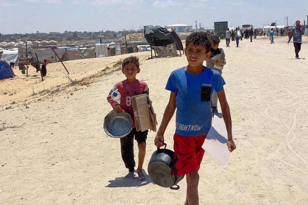Displaced Palestinian children carrying empty pots and cardboard return from an aid distribution center in Khan Yunis in the southern Gaza Strip, on Wednesday. AFP