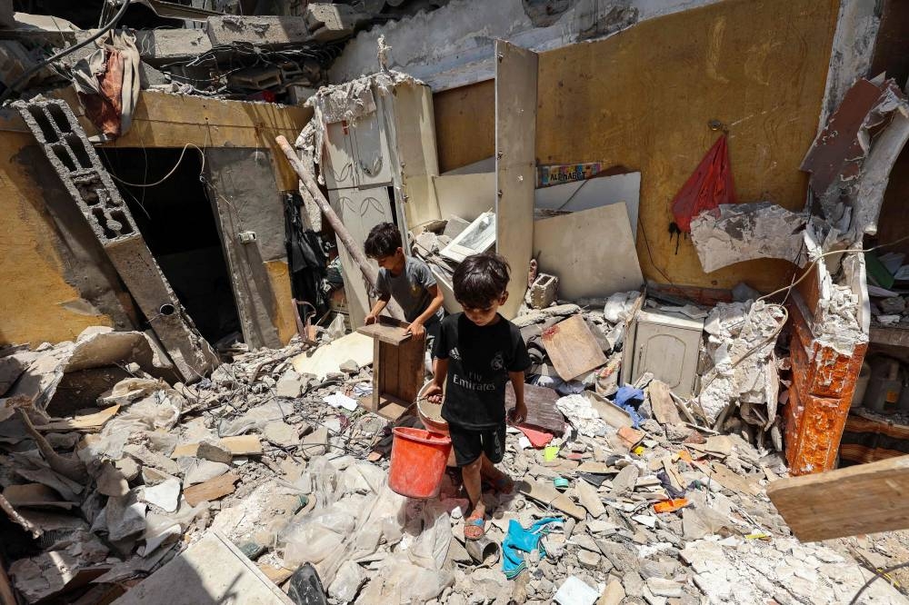 Children carry salvaged items from the rubble of a house targeted in an Israeli strike in the Nuseirat camp in the central Gaza Strip Sunday.