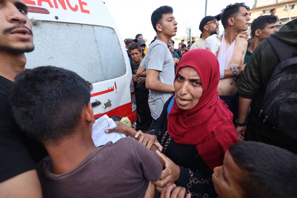 People react as Palestinian rescuers evacuate injured people in an ambulance after an Israeli drone reportedly opened fire on civilian gatherings near an aid distribution point in the central Gaza Strip, on on Sunday, at Bureij camp. AFP