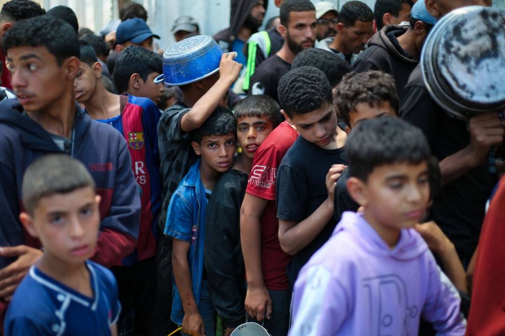 Palestinian children wait with others for food at a distribution point in Nuseirat, central Gaza Strip, on Monday. AFP