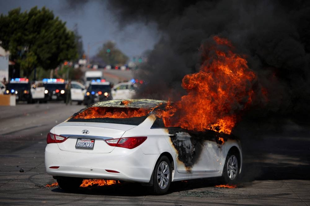 A car burns in flames during a standoff between police and protesters following multiple detentions by Immigration and Customs Enforcement, in the Los Angeles County city of Compton, California, Sunday. REUTERS
