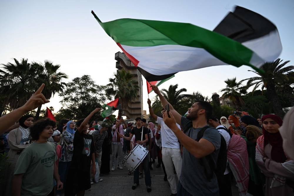 Tunisians wave the Palestinian flag as they gather at a meeting point in Tunis on Monday, ahead of the departure of a land convoy named “Steadfastness” to break the siege on Gaza.  AFP