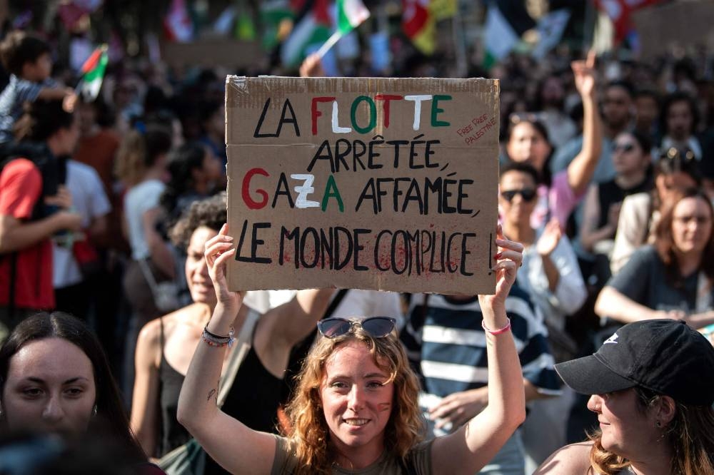 A protestor holds a sign reading "The fleet stopped, Gaza starved, the world complicit" as she attends a demonstration to show her support for activists aboard a boat stopped by Israeli forces enroute to deliver aid to Gaza, in Toulouse, south-western France on Monday. AFP